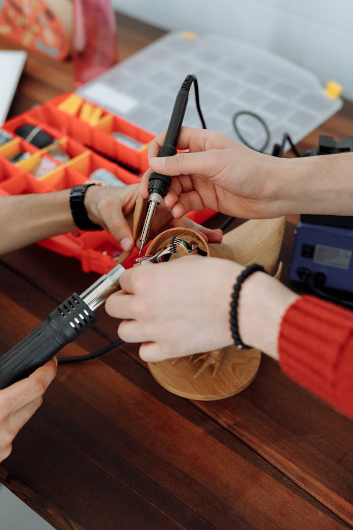 Close-up of hands soldering electronics with tools on a wooden table during a teamwork session.